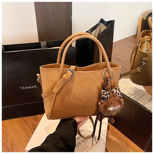 Detail of caramel bucket bag with pebbled leather texture and plush monster charm