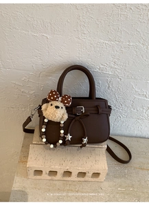 Detail einer dunkelbraunen Mini-Tasche aus Kieselleder mit Plüschwelpen-Anhänger