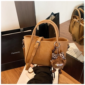 Close-up of warm brown textured leather bucket bag with cute plush monster charm