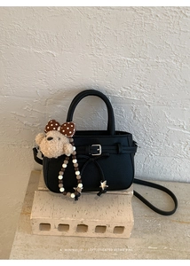 Detail der schwarzen Tasche mit Lychee-Leder, Schleife und Plüschbär-Anhänger