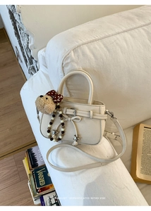 Detail der beige Handtasche mit Schleife, Bärenanhänger und Sternkette auf Sofa
