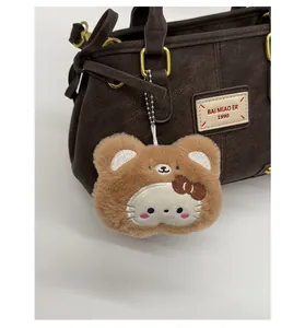 Brown fluffy bear charm with a bow and metal chain on a dark brown leather bag