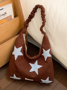 Brown suede tote bag with blue star patch and ruffled shoulder strap in a cozy setting