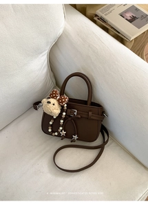 Detail einer dunkelbraunen Handtasche aus Leder mit Plüschbär-Anhänger und Schleife