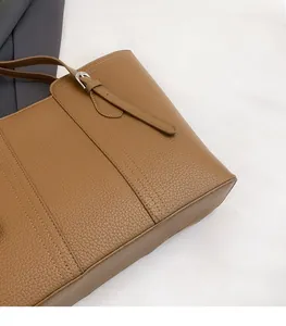 Detailed macro view of brown lychee grain leather tote bag stitching and adjustable buckle