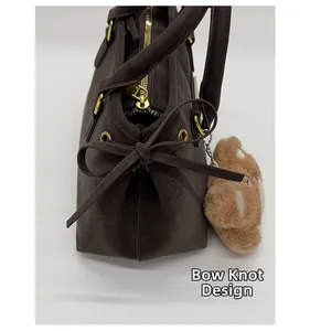 Detail of coffee leather handbag featuring a knotted bow design and golden hardware