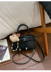 Detail der schwarzen Mini-Vierecktasche mit Bärenanhänger auf einem Holzboden