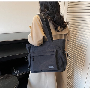 Detail of black nylon tote bag with drawstring side and large front zipper pocket