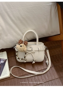Detail einer weißen Handtasche aus Leder mit Schleife und niedlichem Plüschbären-Anhänger