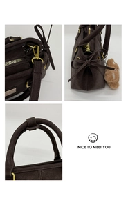 Detail of dark brown tote bag with gold hardware, suede texture and bear charm