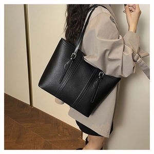 Detail of black pebbled leather tote bag with silver buckle worn on shoulder