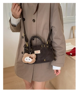 Detail of dark brown corduroy handbag with plush bear charm and brand label