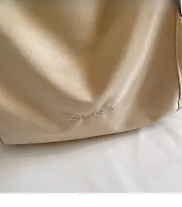 Close-up of embroidered Midolat logo on beige soft leather tote bag texture