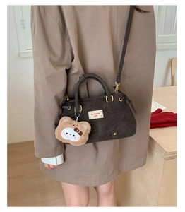 Close-up of a dark grey crossbody bag featuring a cute plush animal charm and logo tag
