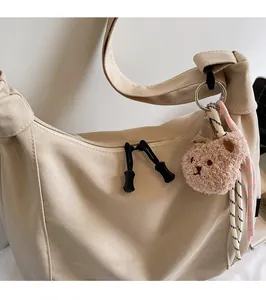 Close-up of beige crossbody bag with durable black zipper and brown plush bear charm