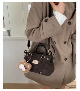 Detail of dark brown corduroy handbag with plush charm and adjustable shoulder strap