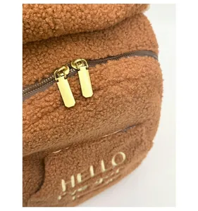 Detail of plush brown teddy fleece fabric with gold HELLO logo and dual metal zippers