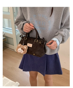 Detail of dark brown suede handbag with brand label and cute plush bear charm