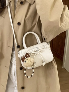 Schicke cremefarbene Handtasche mit Bärenanhänger am Model im khakifarbenen Trenchcoat
