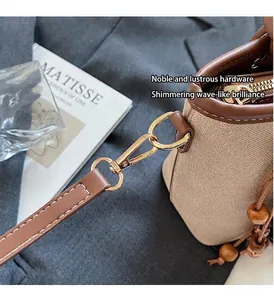 Close-up of canvas and leather bucket bag with gold hardware and wooden bead charm