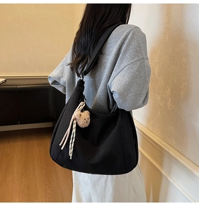Close-up of black canvas crossbody bag with cute plush bear charm and ribbon detail