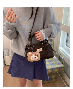 Detail of dark brown corduroy bag with leather handle and cute teddy bear charm