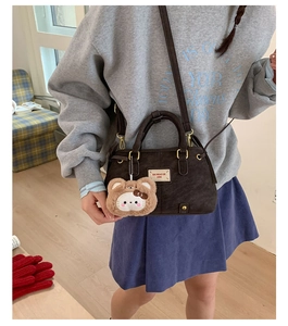 Detail of dark brown matte crossbody bag featuring a bear charm and brand logo plate