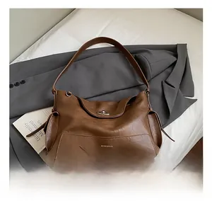 Detailed close-up of brown textured leather tote bag with metal clasp and wide strap