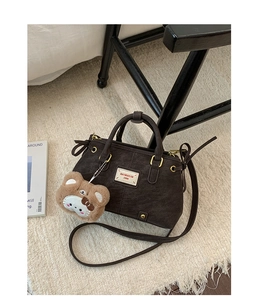 Detail of dark brown vintage faux leather bag with cute plush bear pendant and gold hardware
