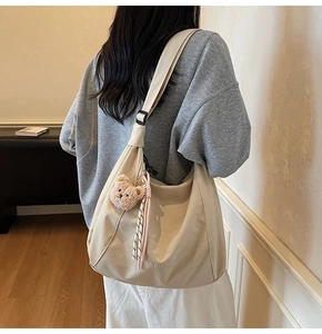 Detail of beige canvas hobo bag with letter embroidery and a brown plush bear charm