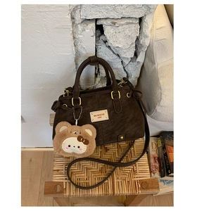 Detail of dark brown pebble leather handbag with vintage label and cute bear charm