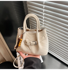 Dettaglio della borsa a tracolla panna con ciondolo in perle di legno e cuciture a V moderne