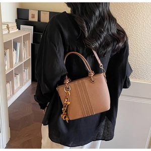 Détail du sac seau en cuir grainé marron avec pendentif en perles porté par le dos