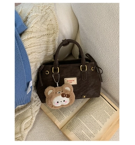 Close-up of deep brown tote bag with logo plaque and cute teddy bear charm on sofa