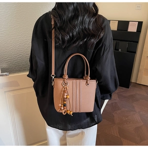 Gros plan du sac seau en cuir marron avec pompon ethnique et détails de perles en bois
