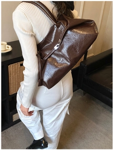 Detail of a large dark brown tote bag in glossy oil-wax leather texture with silver buckle