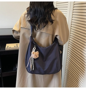 Woman in khaki trench coat carrying a large grey nylon hobo bag with cute bear charm