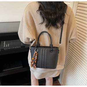 Détail du sac seau noir avec coutures blanches, breloque en perles de bois et anse