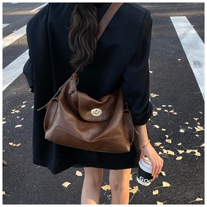 Detail of a large brown leather tote bag with a gold twist-lock on an autumn street