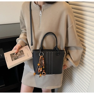 Détail d'un sac seau noir avec surpiqûres blanches et un pendentif rétro en perles de bois