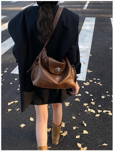 Detail of vintage brown leather tote bag with silver buckle worn by a model in autumn street
