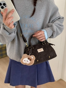 Deep brown vintage tote with crossbody strap and plush cartoon charm in indoor setting