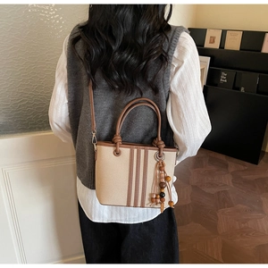 Détail du sac seau en toile avec garniture en cuir marron et pompon en bois