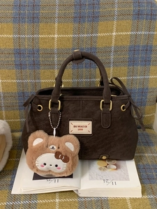 Vintage dark brown suede handbag with gold hardware and plush charm on a plaid background