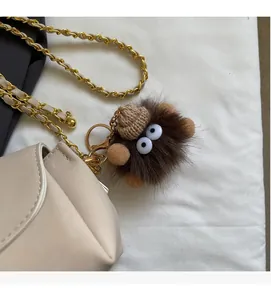 Close-up of cute brown plush keychain with big eyes on beige leather chain crossbody bag