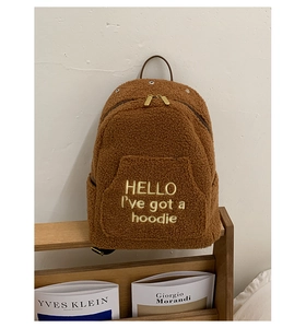 Close-up of brown plush backpack with gold double zippers and hello embroidery