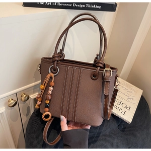 Détail du sac seau marron avec coutures blanches verticales et pompon en perles de bois