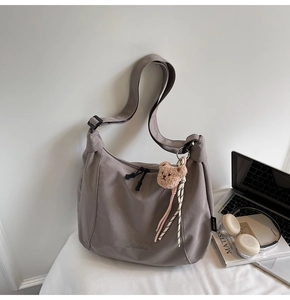 Detail of a dark grey tote bag featuring brand embroidery and a cute teddy bear charm