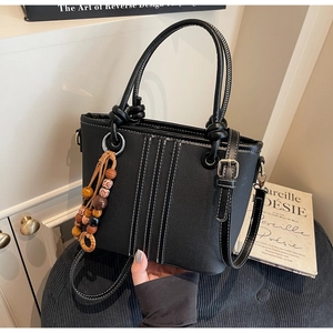 Détail du sac seau noir avec surpiqûres contrastées et pendentif décoratif en perles de bois