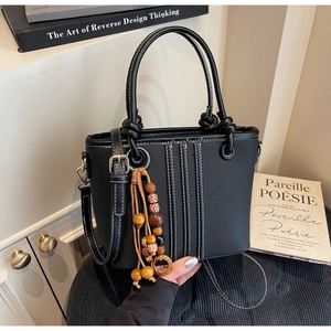 Détail d'un sac cabas en similicuir noir avec coutures blanches et breloque en bois